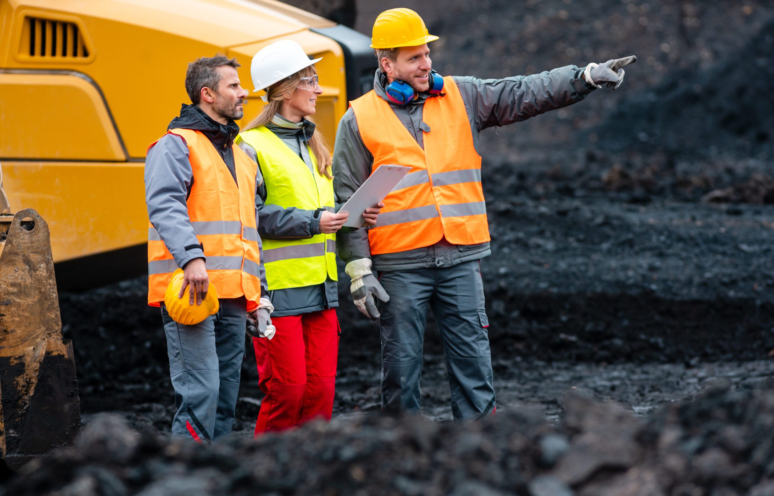 Three workers in quarry with heavy machinery 