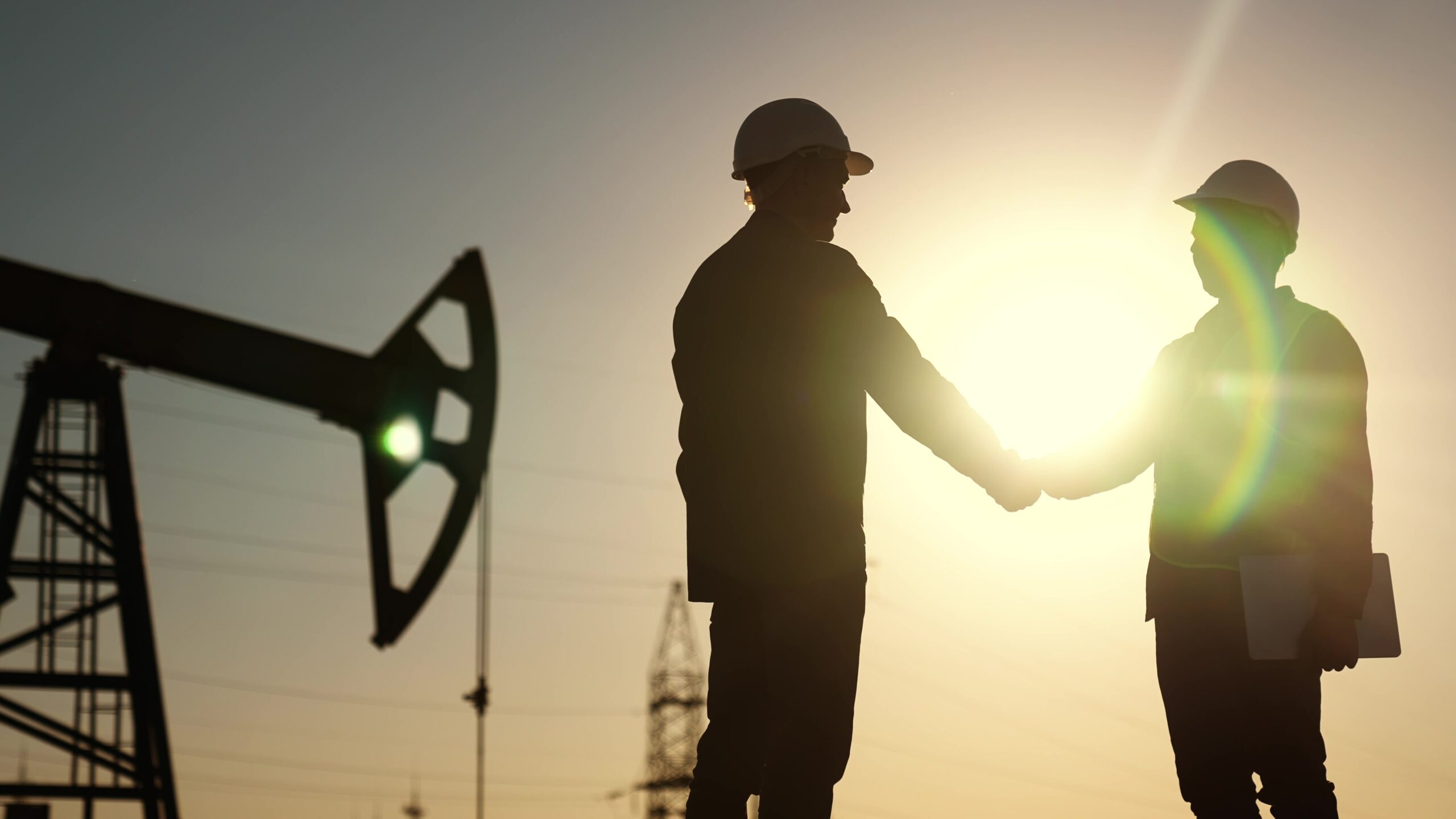 oil business. workers of the fuel industry shaking hands with oil pumps on the lifestyle background. industry business oil and gas concept. engineers of the station handshake silhouette at sunset 